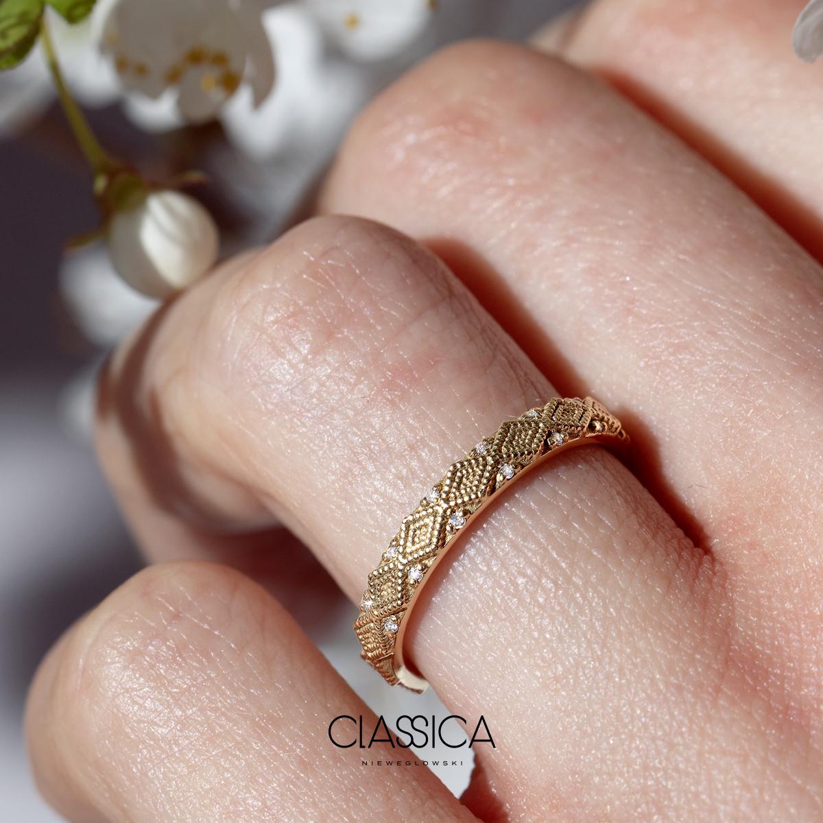 Obrączka ślubna damska w kolorze żółtego złota o szerokości 4mm jest ozdobiona geometrycznym wzorem w kształcie rąbów dookoła obrączki z diamentami pomiędzy przestrzeniami